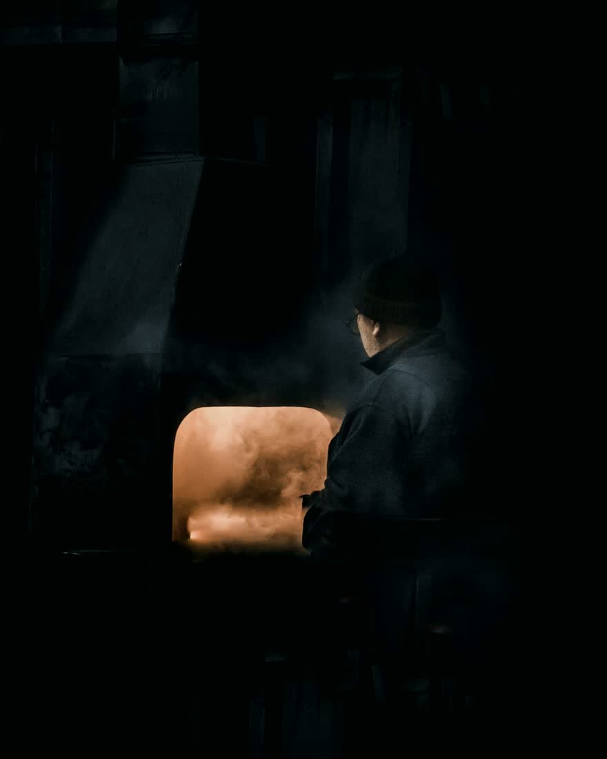 Homme au travail devant un four industriel, dans un atelier faiblement éclairé